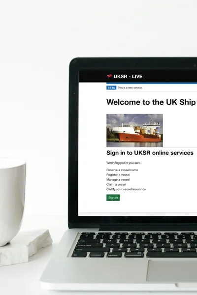 Laptop displaying UK Ship Register Online Service web page with a coffee cup to the left