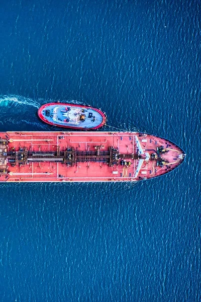 Red tanker with a tug boat at the side of the ship