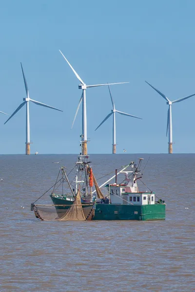 Fishing vessel at sea with offshore wind farm in background