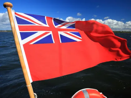 Red ensign UK flag flying at the back of a vessel against blue skies and blue seas