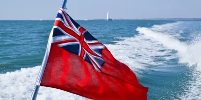 Red Ensign on the back of a vessel with a yacht in the background