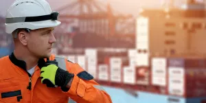 Seafarer looking to the right whilst holding a radio with a container ship in the background