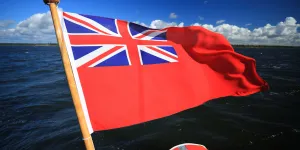 Red ensign UK flag flying at the back of a vessel against blue skies and blue seas