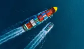Aerial view of container ship being dragged out to sea by a tug boat