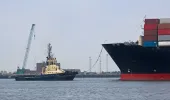 Tug boat on the left with a container ship on the right and a port in the background