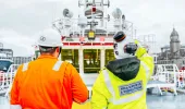 MCA Survey and inspection team member observes a vessel from the deck. They are wearing a yellow hi-visibility jacket and a white hard hat